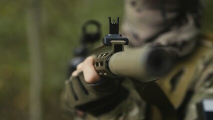 Camouflaged soldier with AR15 carbine. Rifle with a collimator aiming at the camera. Selective focus. Military war recon