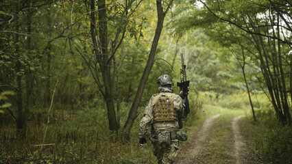 Camouflaged army soldier with AR15 carbine on a mission. Carefully sneaking through a thick green forest and aiming from the rifle. Military recon