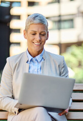 Portrait of a young businesswoman woman using a laptop computer and sitting on a bench in a coty...