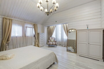 An inviting bedroom features a white wooden interior adorned with soft curtains and elegant furniture. Natural light fills the space, creating a warm atmosphere.