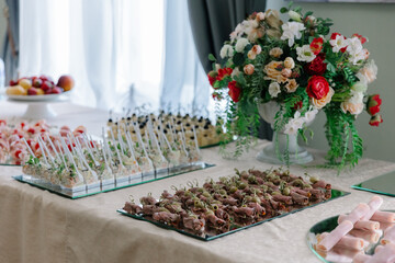 Elegant catering buffet table displaying a variety of gourmet appetizers on mirrored platters, complete with a beautiful, colorful flower arrangement in a bright, airy setting