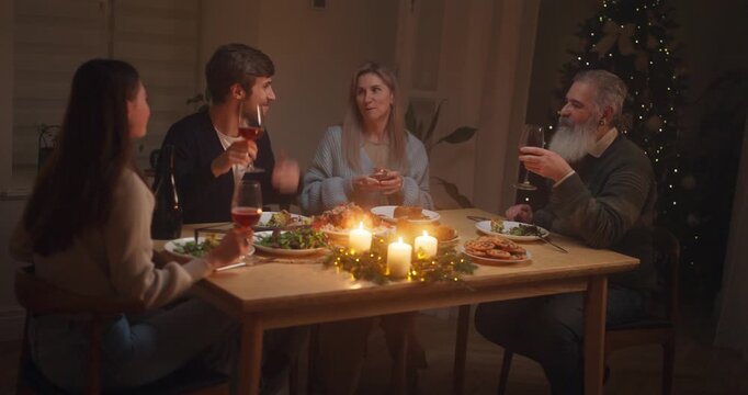 Family gathers around a table to celebrate a festive meal with laughter and toasts in a cozy living room