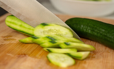 Slicing cucumbers with a large knife on wood cooking board close-up