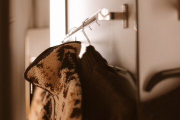 Cozy jacket hanging on a metal rack in a modern interior. A warm fleece jackets hang on a rack, ready for wear, in a sepia-toned room. Warm seasonal clothes in a wardrobe. Warm lighting.