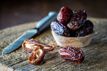 Cut and whole medjool dates on a rustic wooden board against a dark background.