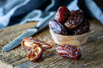 A small wooden bowl of whole medjool dates with a cut one and whole one in front