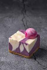 Blueberry and Cream Cheesecake Square with a Marbled Design and Decorative Pink Sphere on a Cracked Stone Surface