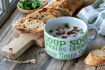 A close up view of a cup of cream of mushroom soup served with crusty bread.