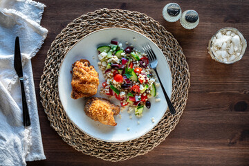A dinner plate of roasted breaded chicken thighs served with couscous salad.