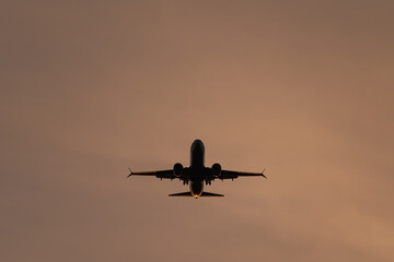 Silhouette of a passenger airplane landing or taking off against a warm, hazy sunset or sunrise sky.