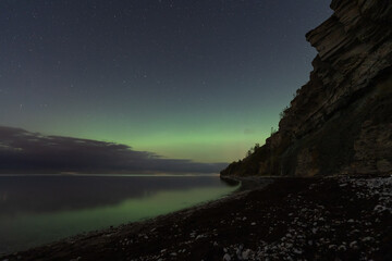 Stunning Northern Lights (Aurora Borealis) over the dramatic Pakri cliff and Baltic Sea in Paldiski, Estonia, under a starry sky.