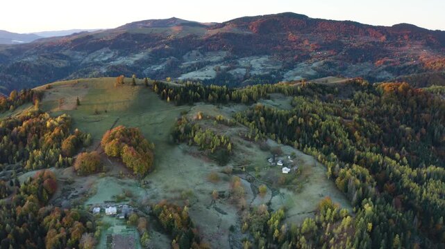 Ukraine, drone, flight in the Carpathians early in the autumn morning at sunrise near the city of Kosiv. Bright forests and dwellings of the Hutsul highlanders on the glades