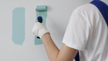 Professional painter holding paint roller, comparing light green paint shades, selecting precise wall color for home renovation, ensuring ideal interior design aesthetic