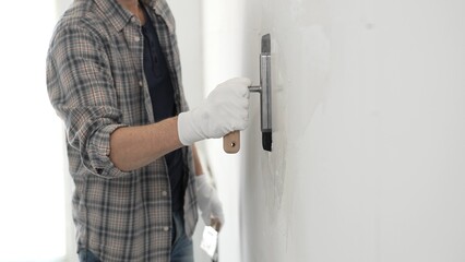 Unknown male construction worker wearing gloves and plaid shirt is using finishing trowel to...