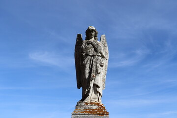 Old statue of an angel with a blu sky. Architecture in a cemetery and religion.