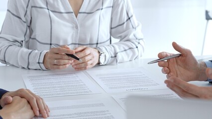 Business professionals or lawyers sitting at the desk in a bright office, reviewing and discussing contract papers. Teamwork concept