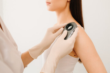 Dermatologist Examining Patient Shoulder with Dermatoscope. Dermatoscopic analysis aids in the...
