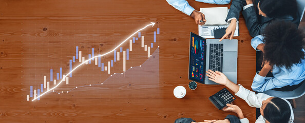 A diverse team engaged in financial analysis, working on a laptop with a graphical chart displayed on a wooden table, emphasizing collaboration and insight. Axiom