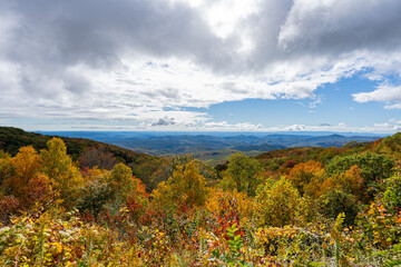 A panoramic view of the Blue Ridge Mountains from the Parkway during peak autumn color, with vibrant foliage stretching beneath dramatic skies.