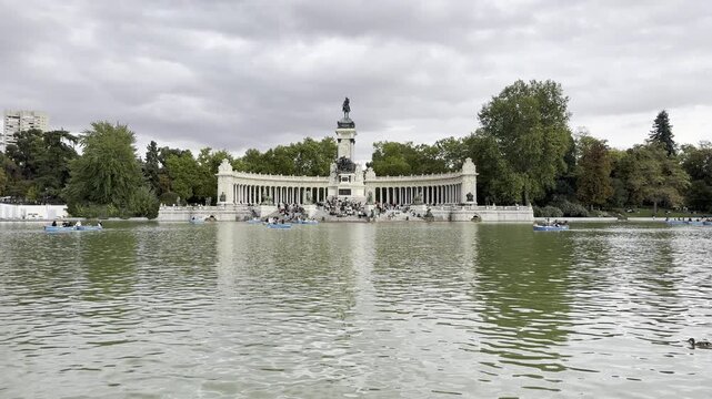Madrid's iconic Retiro Park lake with people relaxing and boating by the Alfonso XII Monument