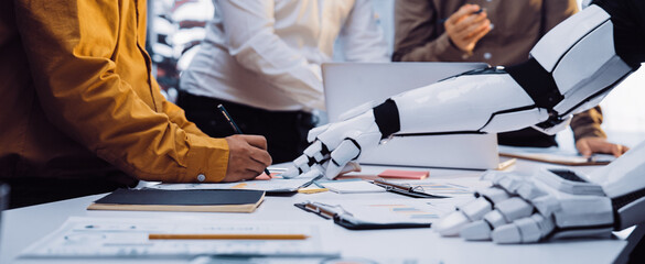 A scene depicting a modern office meeting where a robotic arm assists a human team. This image illustrates advanced technology in collaboration and innovative approaches to teamwork.Noogenesis