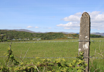 Barbed wired with a concrete post with a field and mountains in the background in Ardara, County Donegal, Ireland