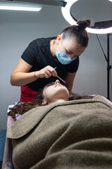 Professional makeup and cosmetology: A lash artist applies eyelash extensions in a studio. Beauty salon: cosmetology procedures
