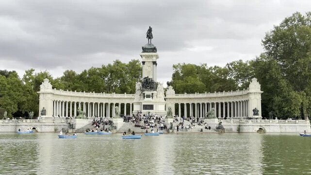 Madrid's iconic Retiro Park lake with people relaxing and boating by the Alfonso XII Monument