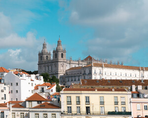 Naklejka premium Historic architecture stands tall over colorful rooftops in Lisbon under a bright blue sky