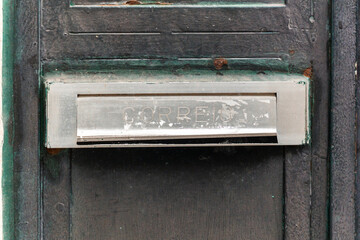 Old mailbox attached to a weathered wooden door with peeling paint in an urban setting