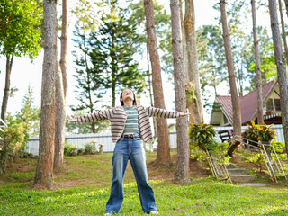 Fototapeta premium Person enjoying nature arms outstretched surrounded by tall trees wearing casual clothing smiling feeling free outdoors bright sunlight green grass peaceful atmosphere