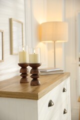 Beautiful LED candles in candlesticks on wooden chest of drawers indoors. Space for text