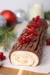 Delicious Yule log (traditional Christmas cake) with redcurrant, decor and fir tree branches on table, closeup