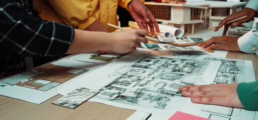 A dynamic scene showcasing a collaborative office environment where multiple individuals engage in project design using blueprints and creative tools, fostering teamwork and innovation. SACTR