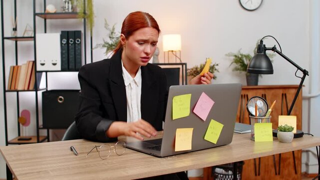Young businesswoman at home office stares at sticky note covered laptop stressed by piling chores. Freelancer girl at table rips notes away fearing unfinished goals and racing clock before day ends