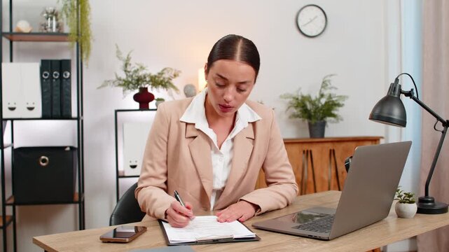 Young businesswoman at home office checks paper bills frowns at total takes photo and marks error lines. Freelancer girl at table writes note for accountant adds bill id and saves photos to folder