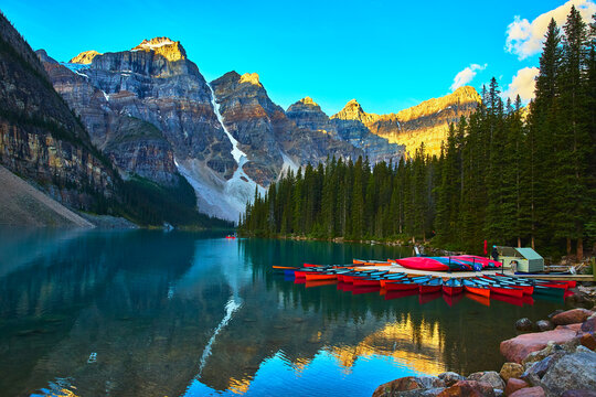 Canoes on Crystal Lake at Sunrise with Majestic Mountains and Pine Forest Reflections
