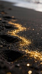 Golden glitter scattered on dark sand near shoreline with footprints