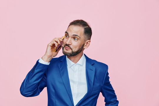 A focused business man in a blue suit on a pink background speaks on a mobile phone, projecting confidence and concentration while isolated from surroundings.