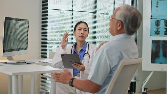 Asian female doctor discussing symptoms, health consulting senior elderly male patient in clinic, using digital tablet to record and analyze medical data. Modern healthcare with integrated technology.