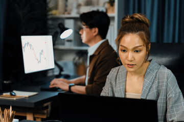Serious face of thinking businesswoman focusing computer to report data analysis social media online project job with coworker working at back side at over late night time at modern office. Infobahn.