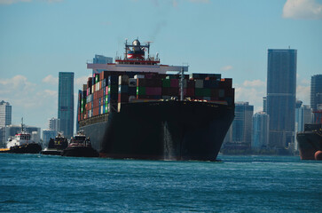 Tug boats maneuvering a container ship into a loading dock at the Port of Miami.