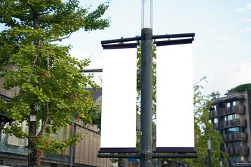 Blank vertical advertising banners double hanging posters by the road, against lush green trees and plants. Mock up.