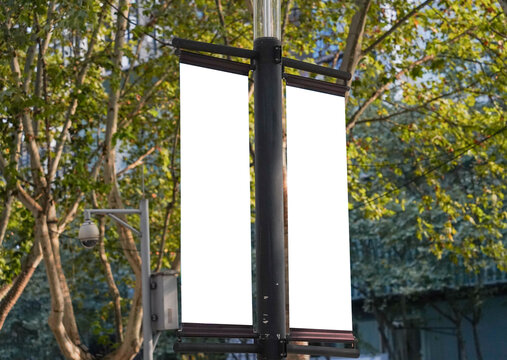 Blank vertical advertising banners double hanging posters by the road, against lush green trees and plants. Mock up.