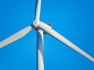 A macro detailed photograph of the central hub and rotor of a modern wind turbine showcasing the engineering and design of the giant blades against a clear blue background