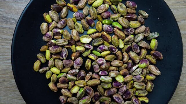 Black plate filled with unshelled pistachios on a wooden surface