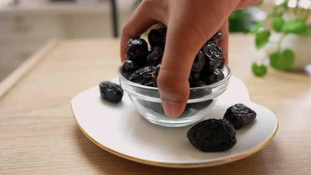 Hand picking dried prunes from a glass bowl on a wooden table