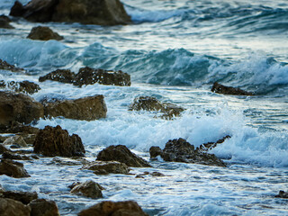 A beautiful and chaotic scene of choppy sea waves breaking over a rocky coastline creating a dynamic texture of white foam and blue water