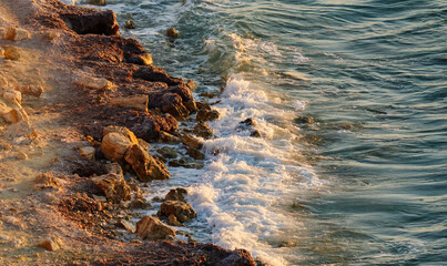 A beautiful vertical shot of a sandy and rocky coastline with gentle sea waves washing ashore during the warm light of golden hour
