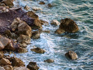 A stunning photograph of a large turquoise sea wave curling and breaking with white foam as it moves powerfully towards the dark rocks on the shore
